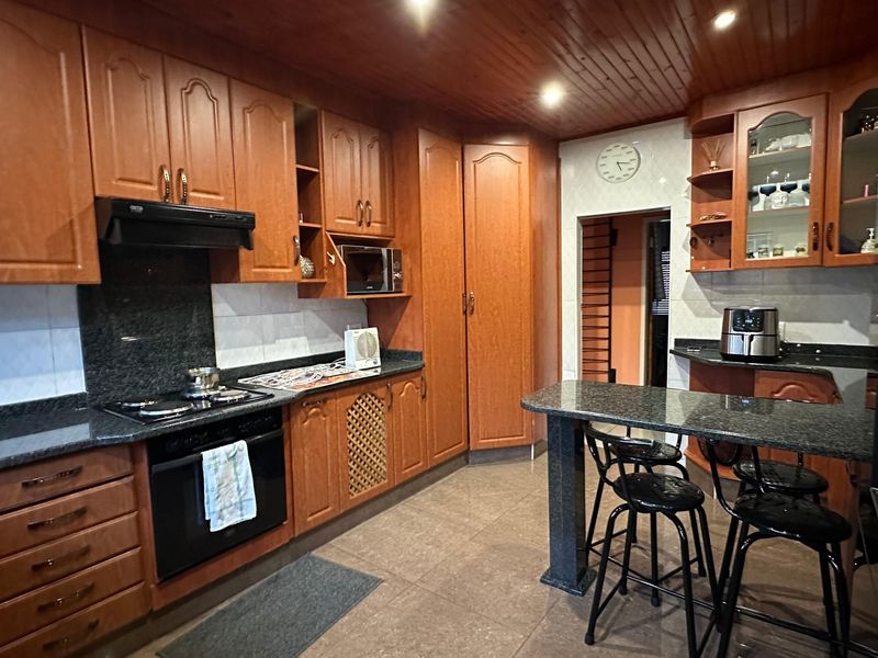 A traditional kitchen featuring warm timber cabinetry, granite countertops, built-in appliances, and a timber-clad ceiling with recessed lighting.
