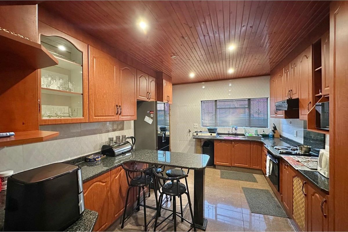 A functional kitchen featuring extensive wooden cabinetry, granite countertops, a built-in oven, hob, and a distinctive timber-clad ceiling with recessed lighting.