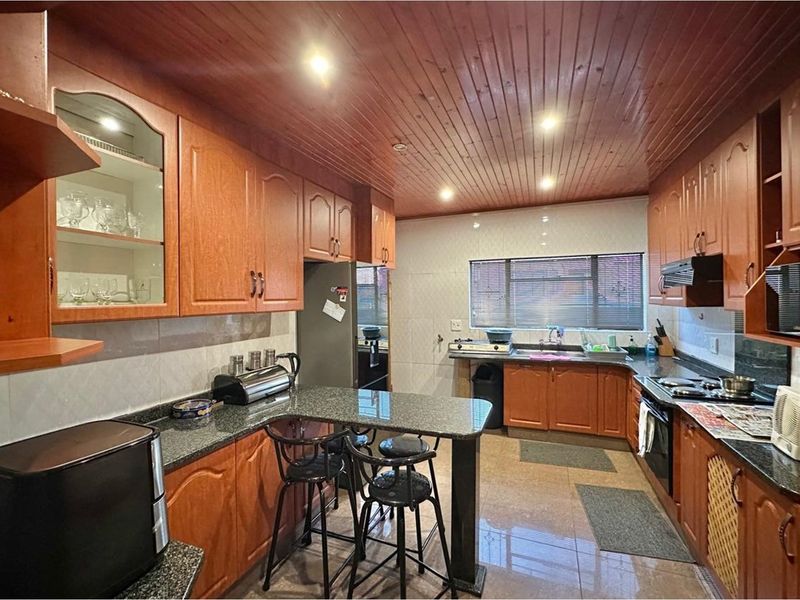 A functional kitchen featuring extensive wooden cabinetry, granite countertops, a built-in oven, hob, and a distinctive timber-clad ceiling with recessed lighting.