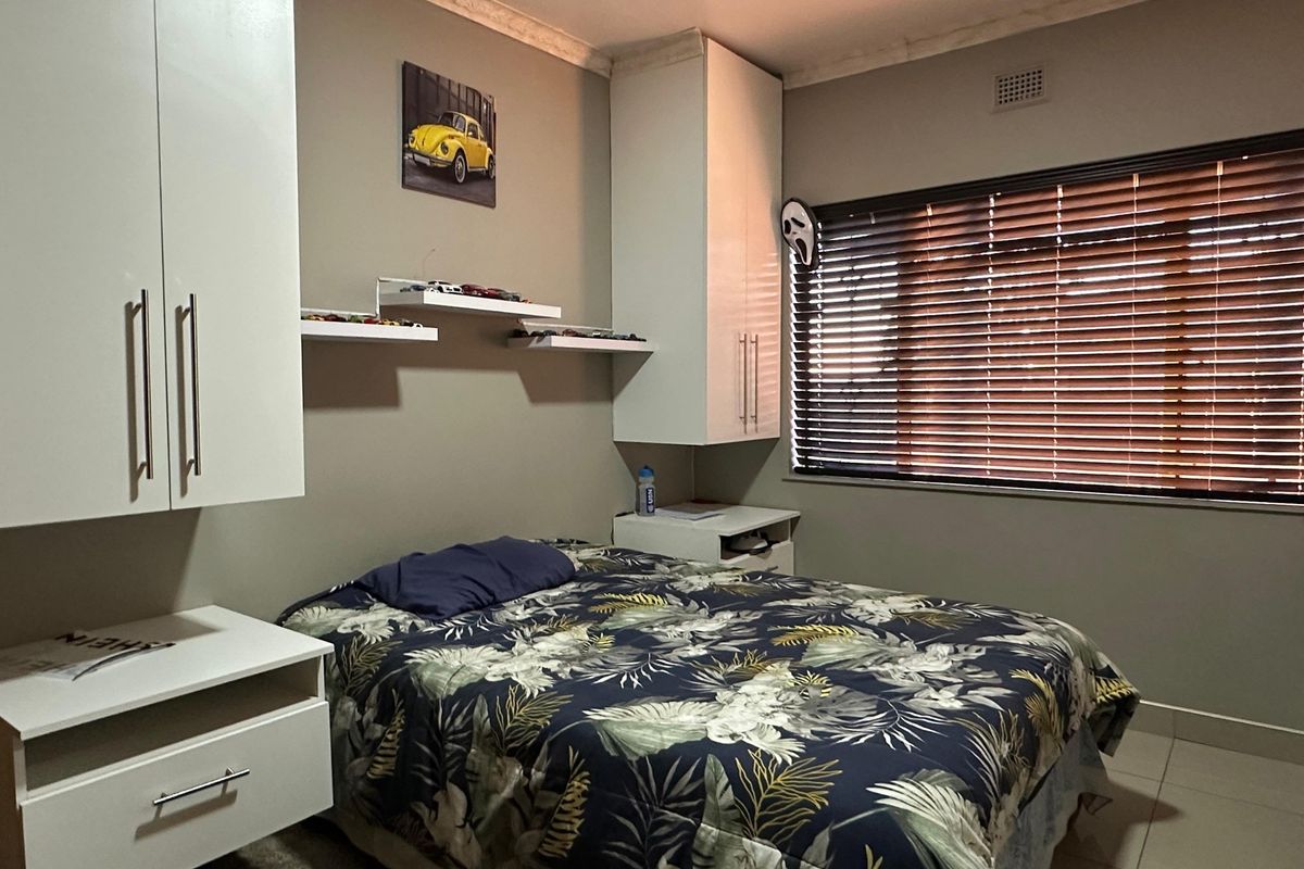 A functional bedroom featuring built-in white cabinetry, floating shelving, tiled flooring, and venetian blinds for light control.