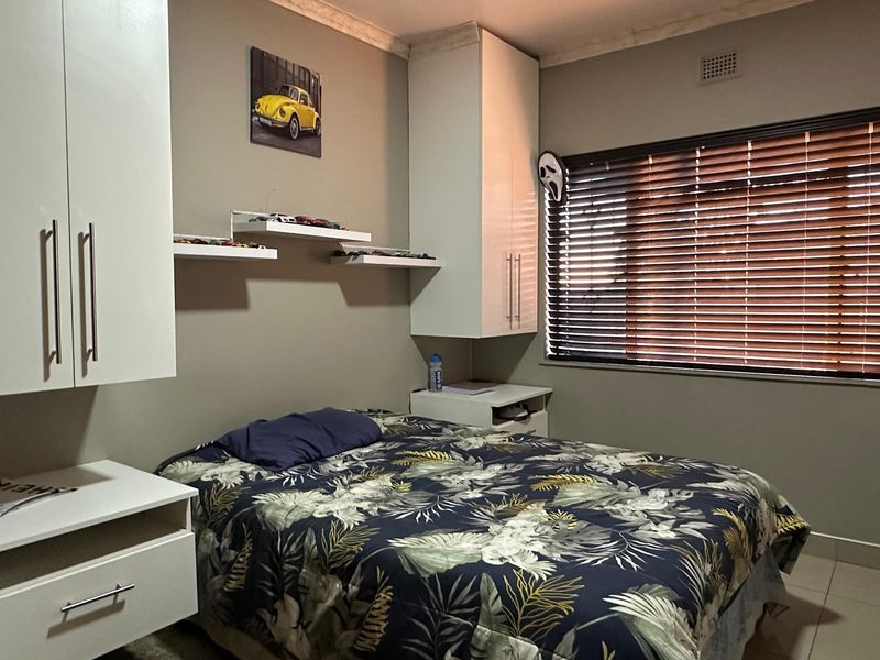 A functional bedroom featuring built-in white cabinetry, floating shelving, tiled flooring, and venetian blinds for light control.