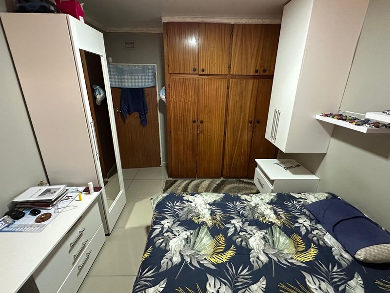 A functional bedroom featuring built-in wooden cupboards, tiled flooring, and neutral wall finishes, providing ample storage and a clean, practical layout.