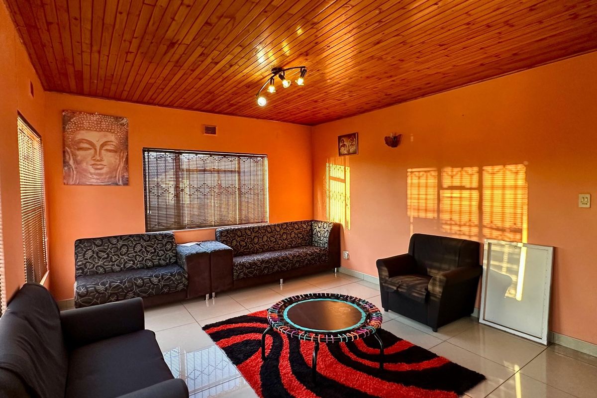A living room featuring a warm timber tongue and groove ceiling, tiled flooring, and large windows with fitted venetian blinds.