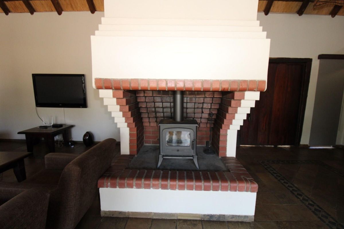 A spacious living area featuring a prominent central brick fireplace with a built-in wood-burning stove and exposed timber ceiling beams.