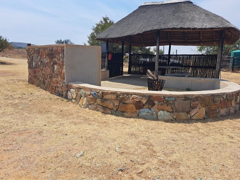 Outdoor thatched lapa area featuring a stone masonry wall and built-in braai, perfect for entertaining in a natural setting.