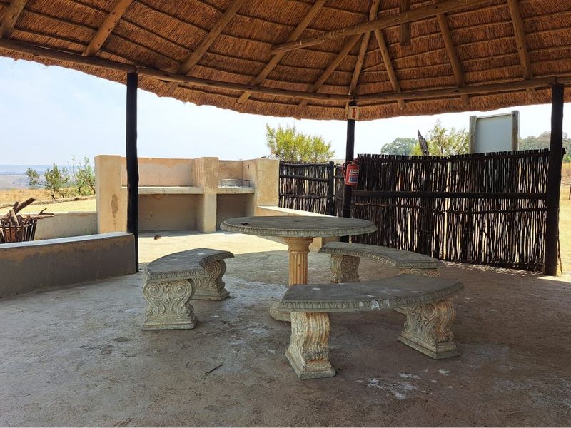 Covered outdoor entertainment area featuring a thatched roof, built-in braai, and rustic concrete seating, ideal for relaxed outdoor gatherings.