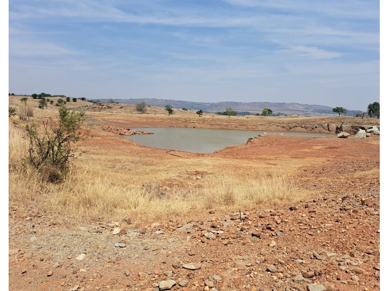 A wide view of the vacant residential land featuring natural rocky terrain and a small dam.