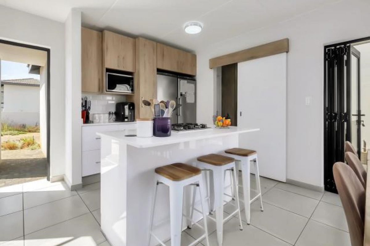 Modern kitchen featuring a central island with a built-in gas hob, light wood cabinetry, and tiled flooring, with direct access to an outdoor patio area.
