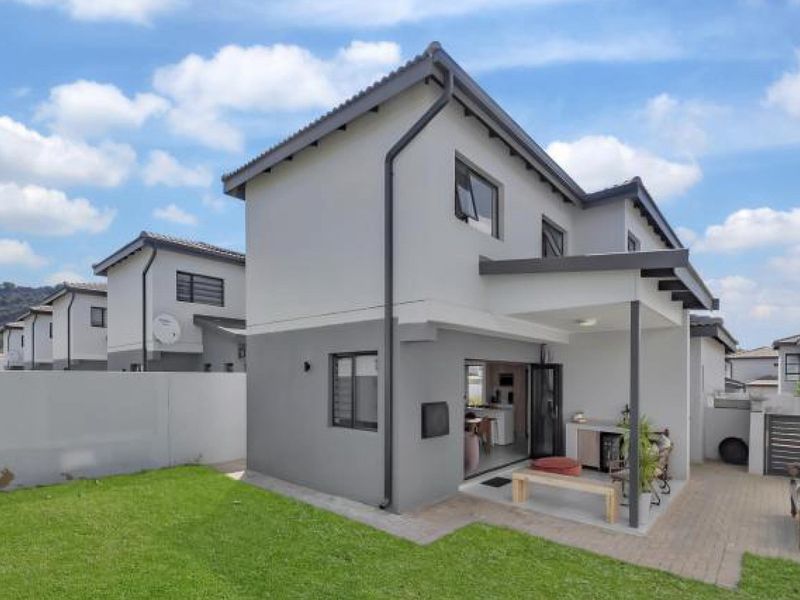 Rear view of the townhouse featuring a covered patio, paved outdoor space, and a private lawn area enclosed by boundary walls.
