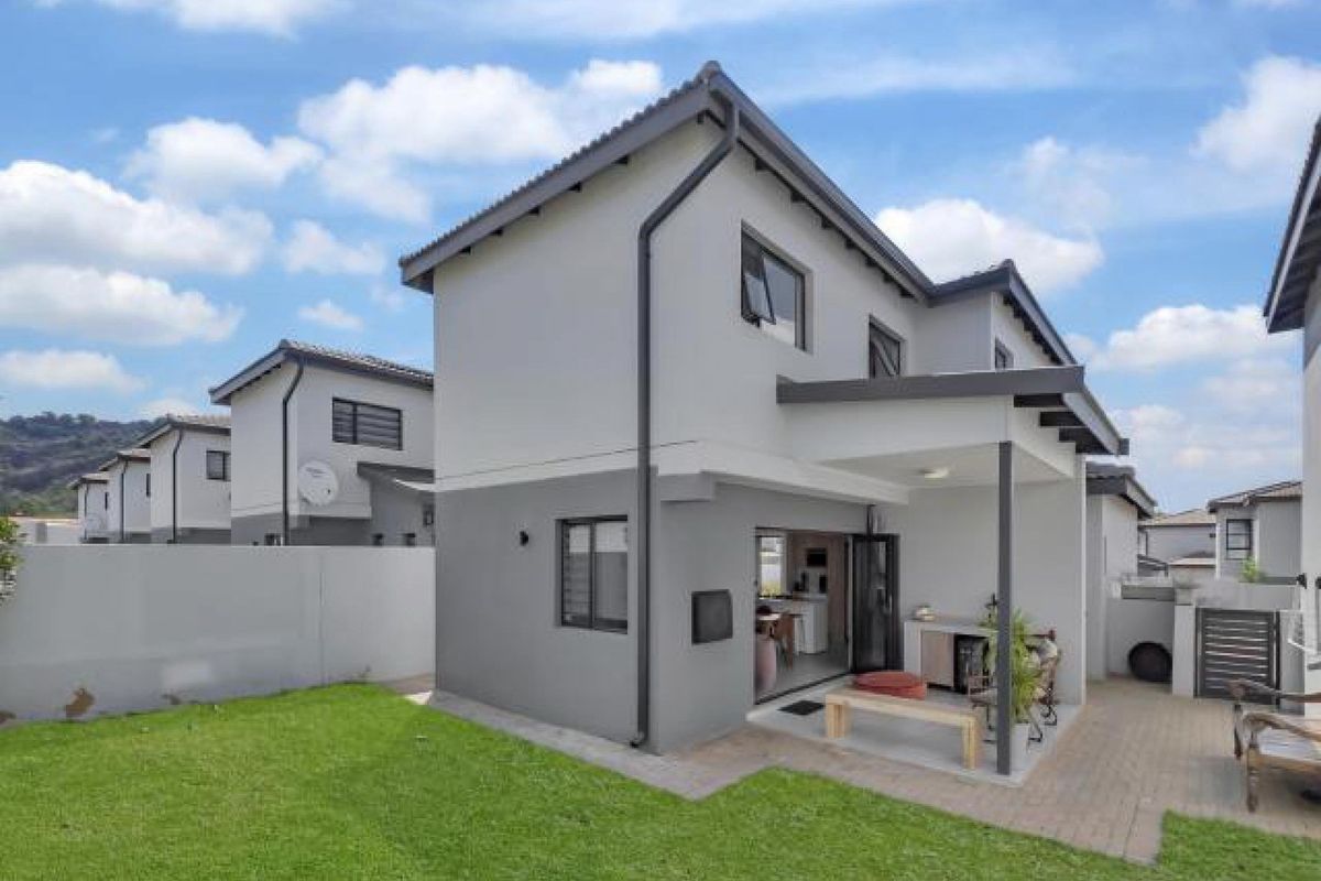 Rear view of the townhouse featuring a covered patio, paved outdoor space, and a private lawn area enclosed by boundary walls.