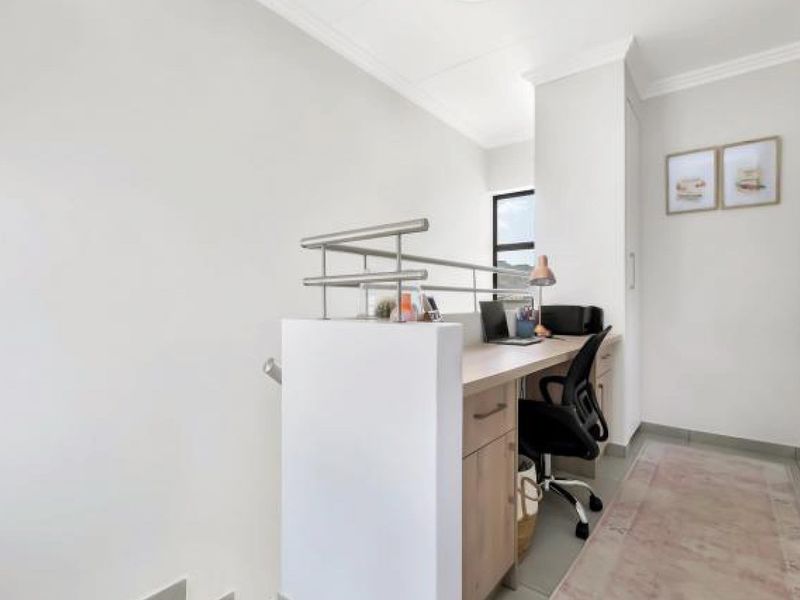 A compact home office area featuring a built-in desk with integrated cabinetry and a modern metal balustrade overlooking the staircase.