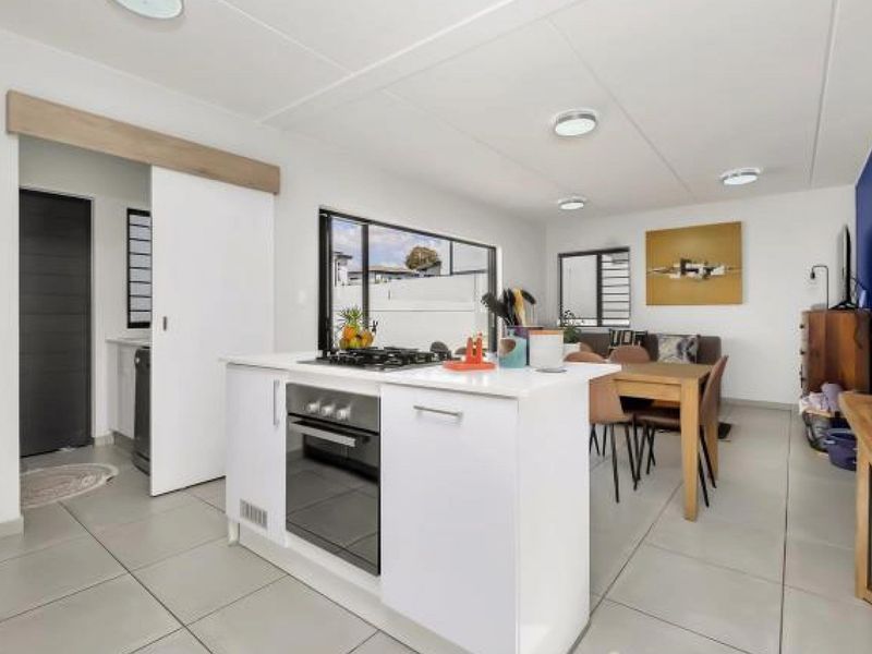 Modern open-plan living area featuring a central kitchen island with built-in oven and gas hob, complemented by sleek tiled flooring and neutral finishes.