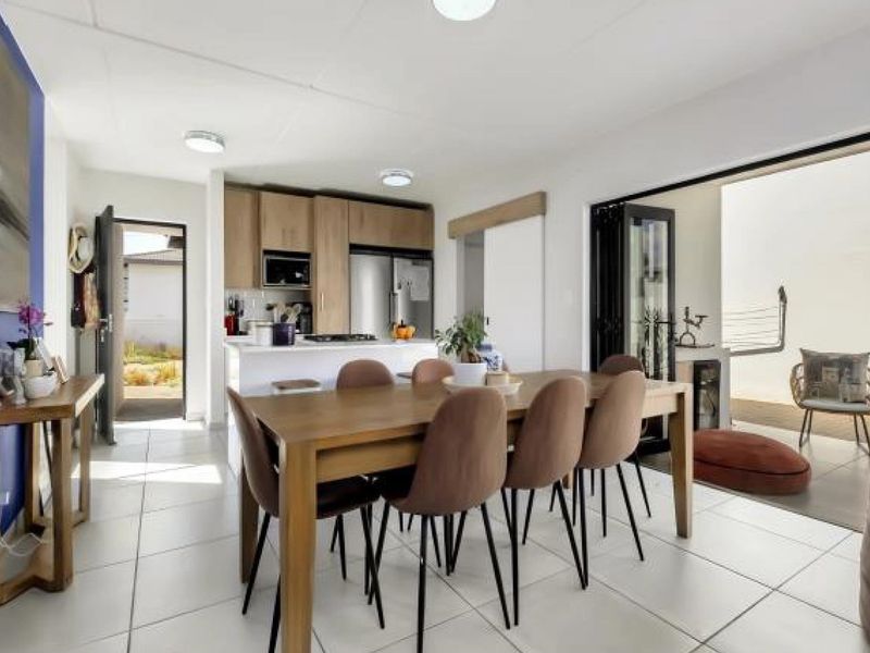 Open-plan living and dining area featuring tiled floors, modern kitchen cabinetry with built-in appliances, and seamless access to an outdoor patio through bi-fold doors.