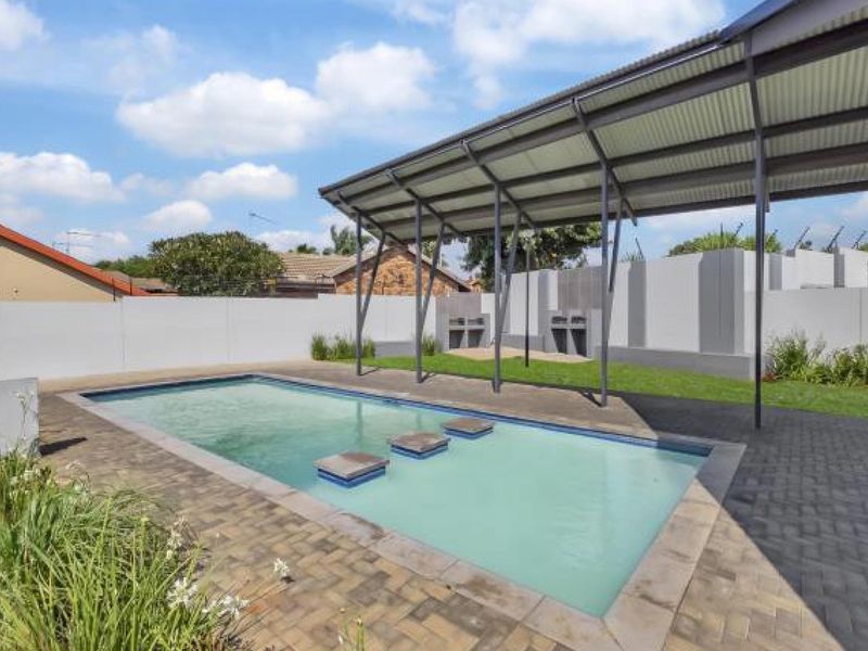 Outdoor pool area featuring a swimming pool with stepping stones, a covered patio structure, and built-in braai facilities within a walled garden.