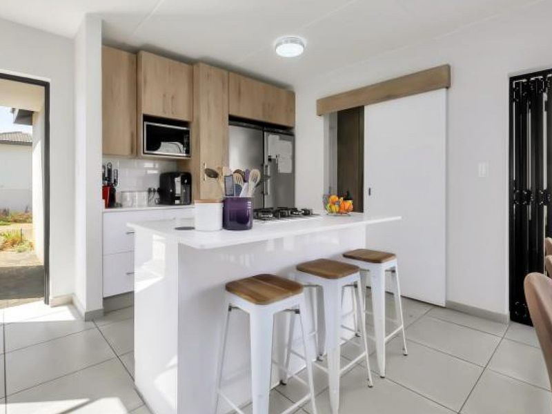 Modern kitchen featuring a central island with a gas hob, light wood cabinetry, and tiled flooring, with direct access to an outdoor patio area.