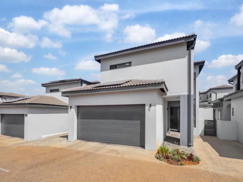 Modern townhouse exterior featuring a clean grey facade, tiled roof, and a spacious sectional garage with paved driveway access.