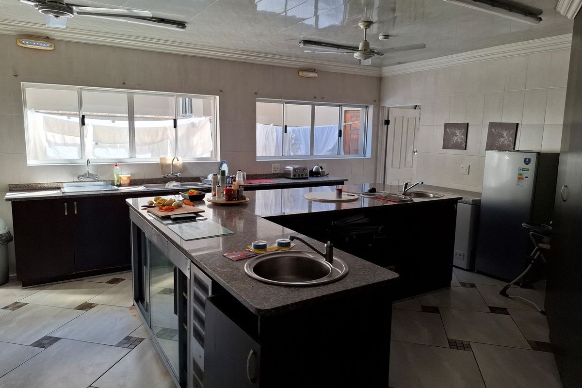 Spacious kitchen featuring a large central island with granite countertops, double sinks, extensive cabinetry, and tiled finishes throughout.