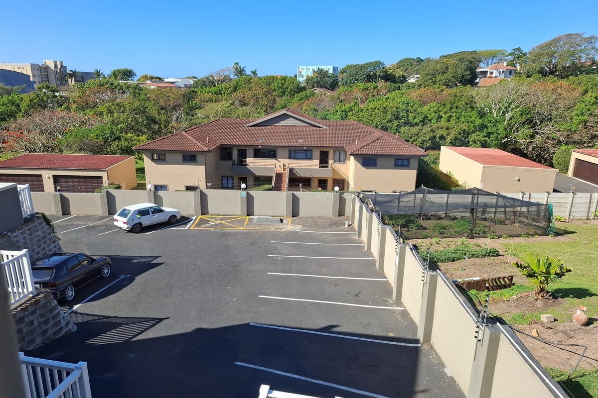 An elevated aerial view of the property complex, featuring a paved parking area, perimeter wall with electric fencing, and surrounding landscaped grounds.