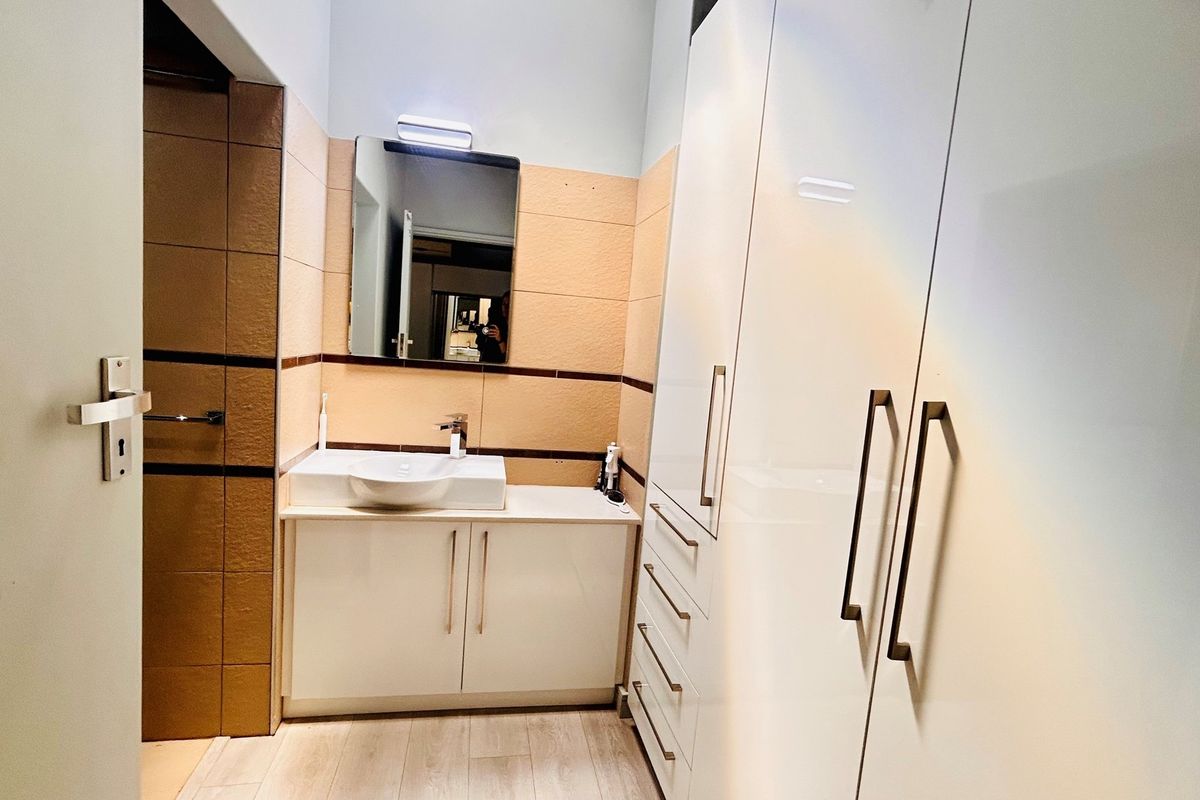 A modern bathroom featuring a vanity with a vessel sink, wall-mounted mirror, and built-in floor-to-ceiling storage cabinetry.
