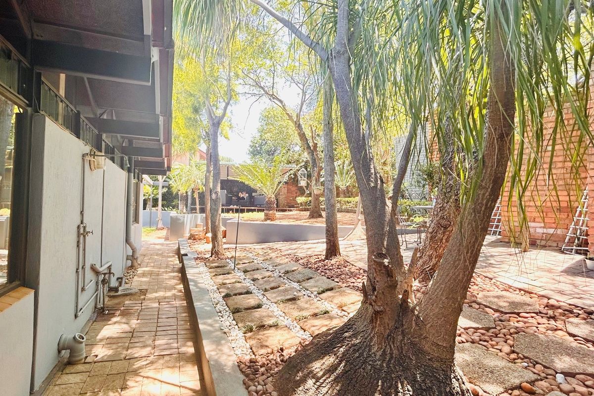 A spacious rear garden area featuring mature trees, paved walkways, and a mix of stone and brick landscaping elements.