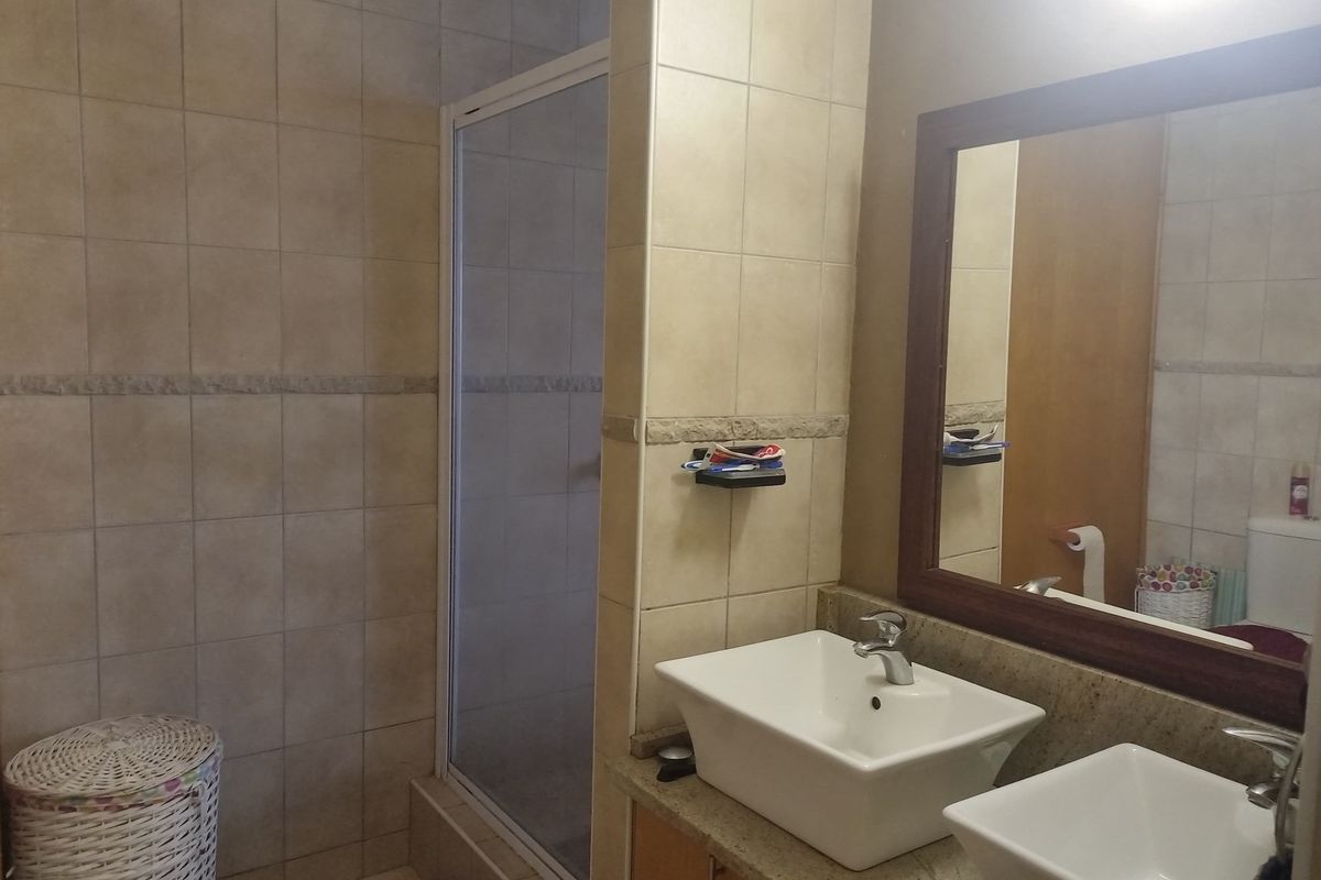 A functional bathroom featuring a double vanity with vessel sinks, a framed mirror, and a glass-enclosed shower stall with tiled walls.