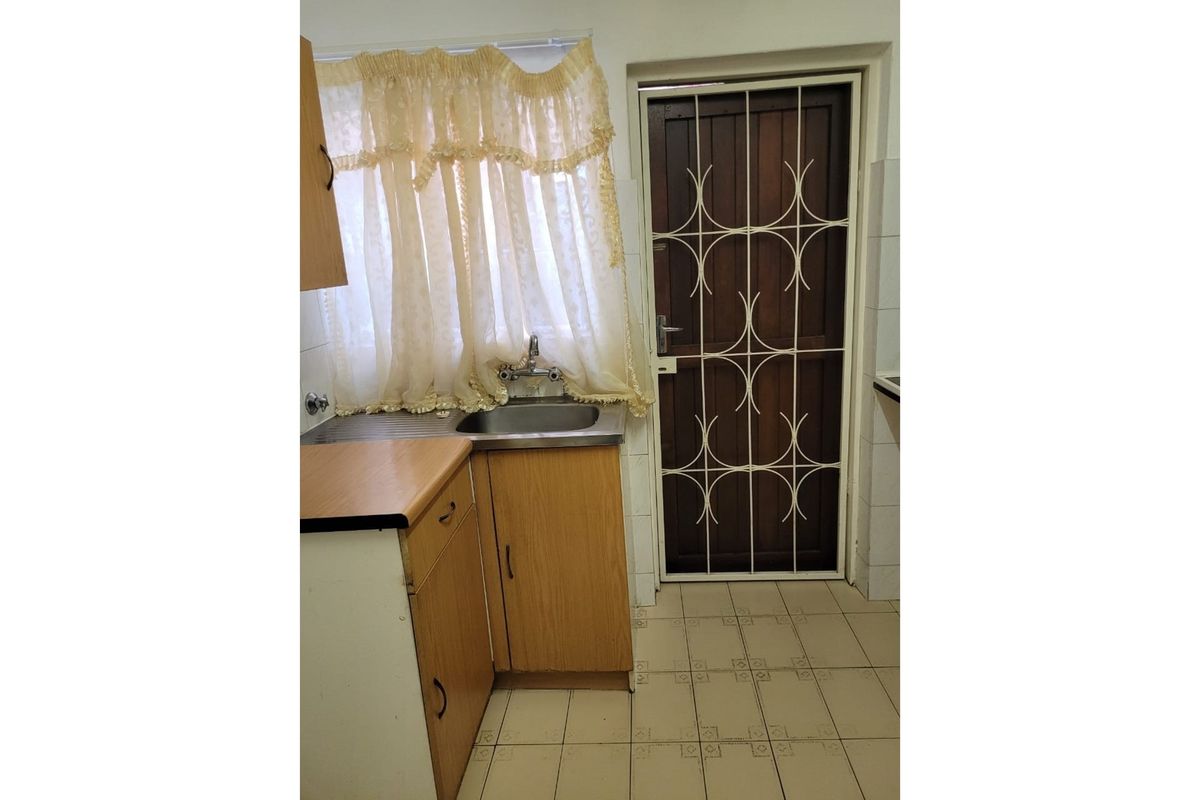 A compact kitchen area featuring wooden cabinetry, laminate countertops, a stainless steel sink, and a secure exterior door with a metal security gate.