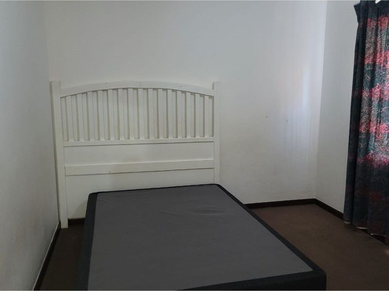A simple bedroom featuring plain walls and carpeted flooring, providing a blank canvas for potential interior updates.