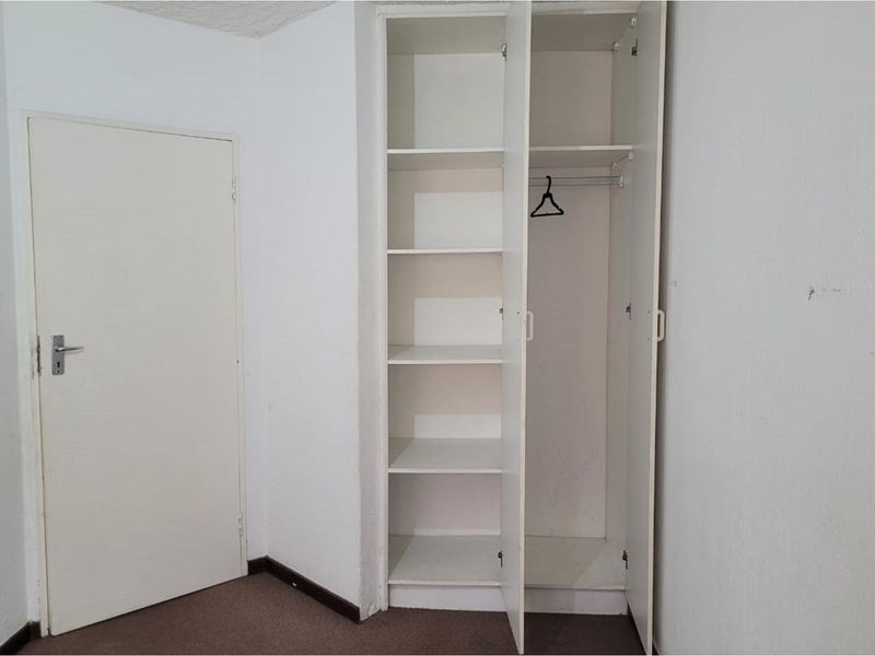 A vacant bedroom featuring a built-in wardrobe with shelving and hanging space, finished with neutral walls and carpeted flooring.