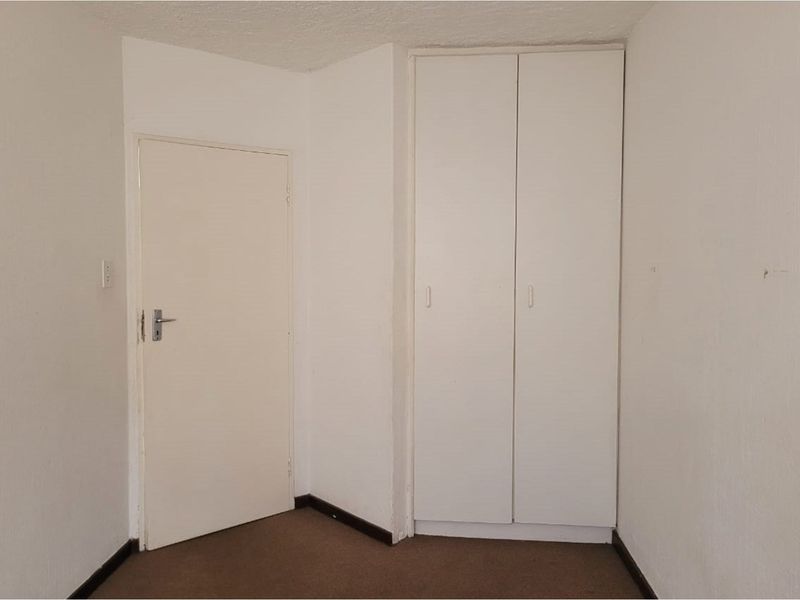 An empty bedroom featuring a built-in wardrobe, carpeted flooring, and neutral white walls, offering a blank canvas for personalization.