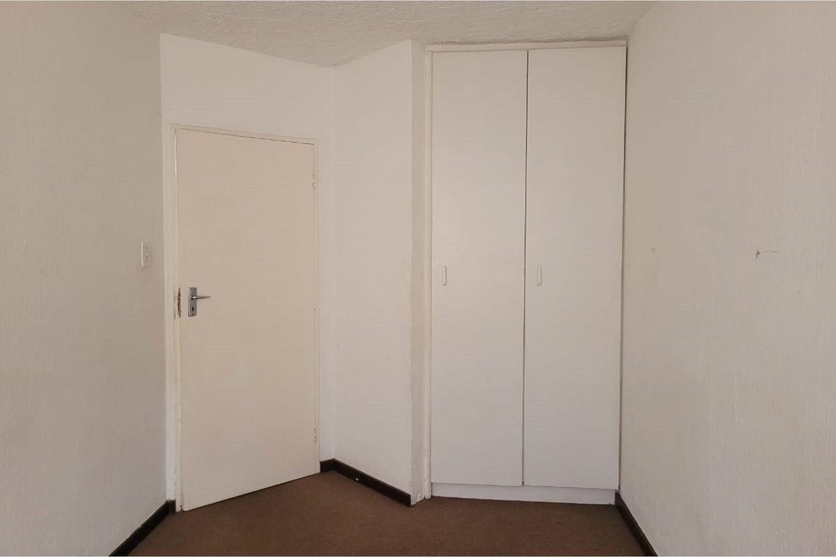 An empty bedroom featuring a built-in wardrobe, carpeted flooring, and neutral white walls, offering a blank canvas for personalization.