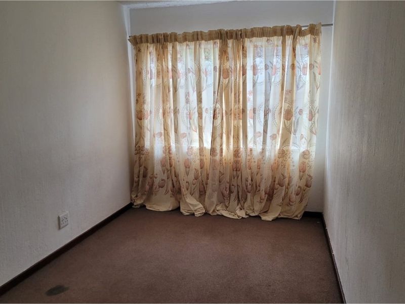 An empty bedroom featuring carpeted flooring and a window with curtains, presenting a blank canvas for potential renovation or restyling.
