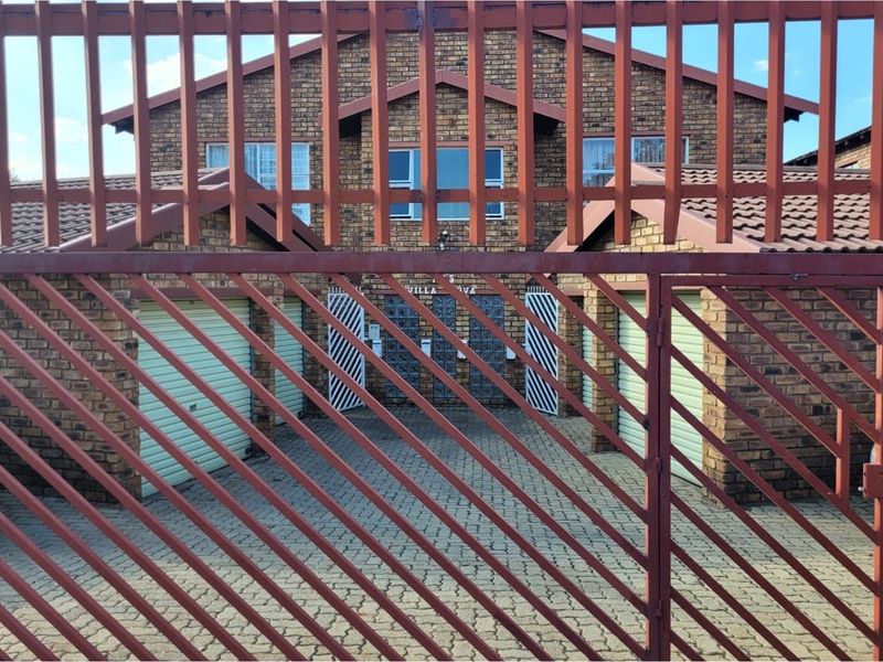 Front view of the apartment complex featuring a brick facade, paved driveway, and secure metal gate access with integrated garage units.