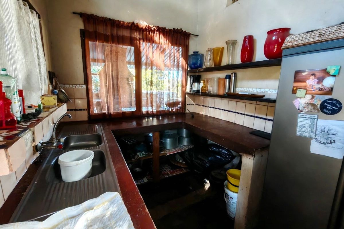A functional kitchen area featuring a double-basin stainless steel sink, tiled splashbacks, and open-shelf storage configuration.