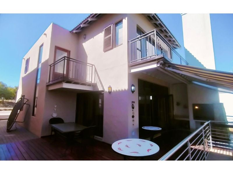 Rear exterior view of a two-story house featuring a wooden deck, multiple balconies with metal railings, and a retractable awning over the patio area.