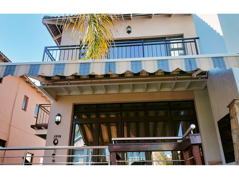 Rear exterior view featuring a covered patio with a retractable striped awning, a balcony above, and large glass sliding doors.