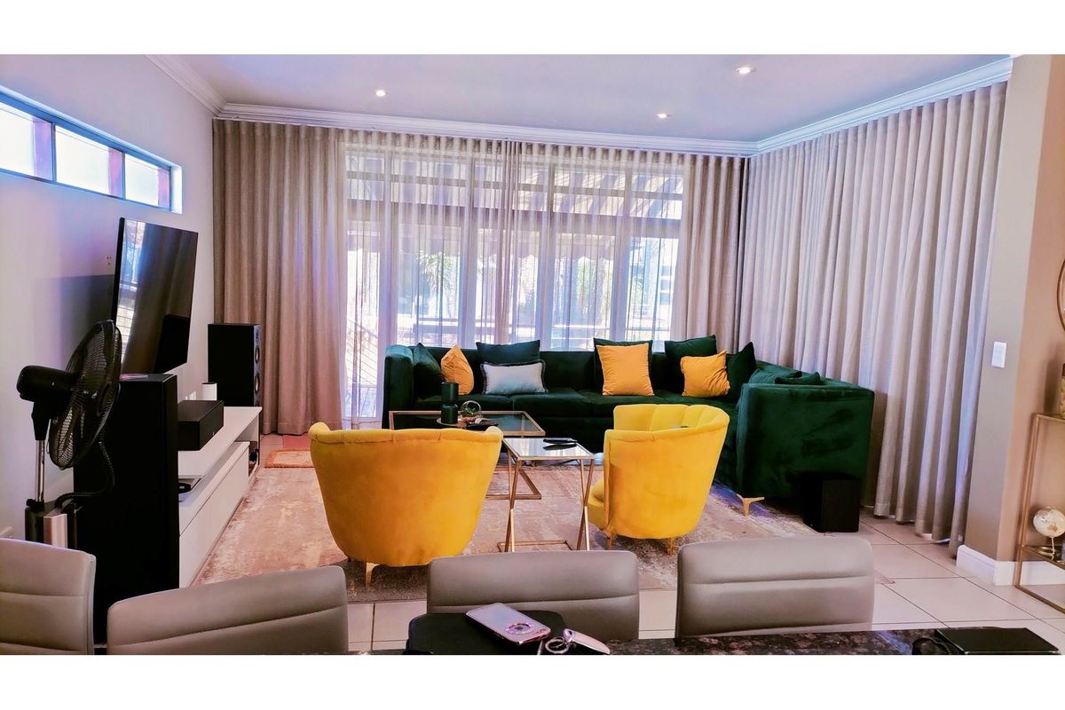 A well-maintained living room featuring recessed ceiling lighting, floor-to-ceiling curtains, and large glass sliding doors leading to an outdoor area.