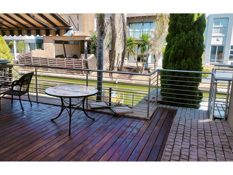 A canal-facing patio featuring timber decking, stainless steel balustrades, and a retractable awning, offering a pleasant outdoor entertainment space.