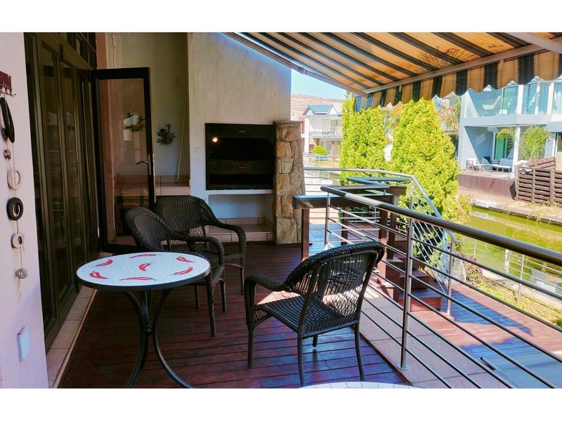 Covered patio area featuring a built-in braai, timber decking, and stainless steel balustrades overlooking the canal.