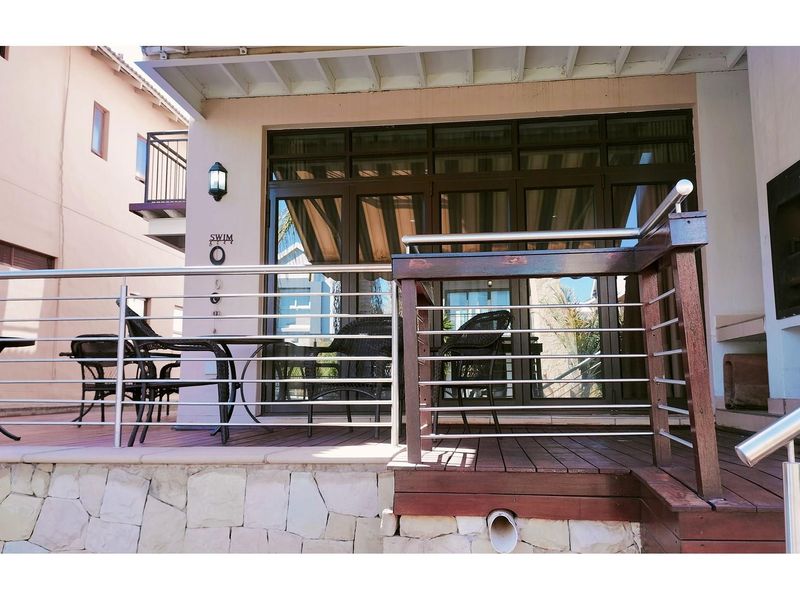 A covered patio area featuring timber decking, stainless steel balustrades, and large glass sliding doors leading into the main living space.