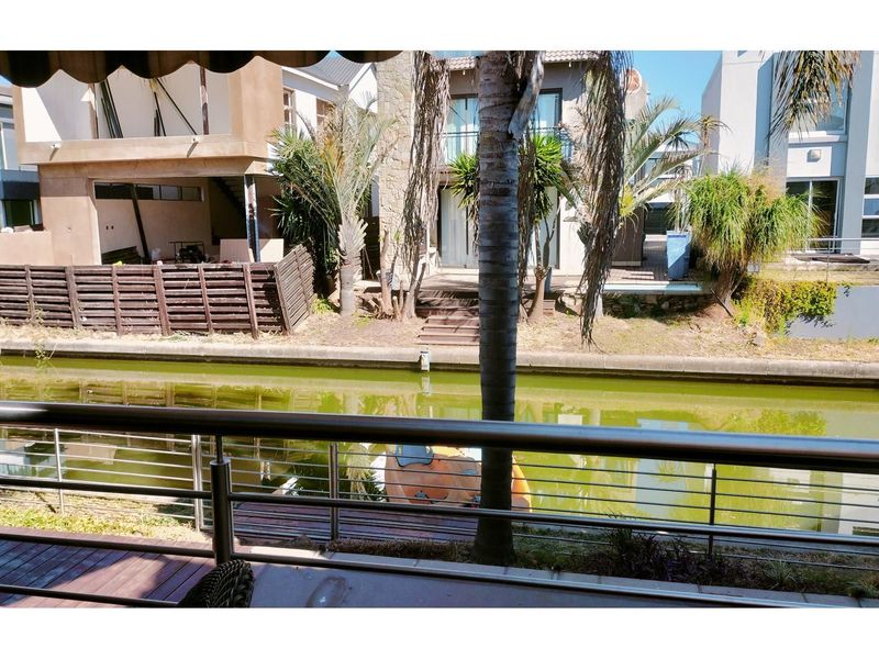 View from a balcony overlooking a canal, featuring stainless steel railings and timber decking, with neighboring residential properties in the background.
