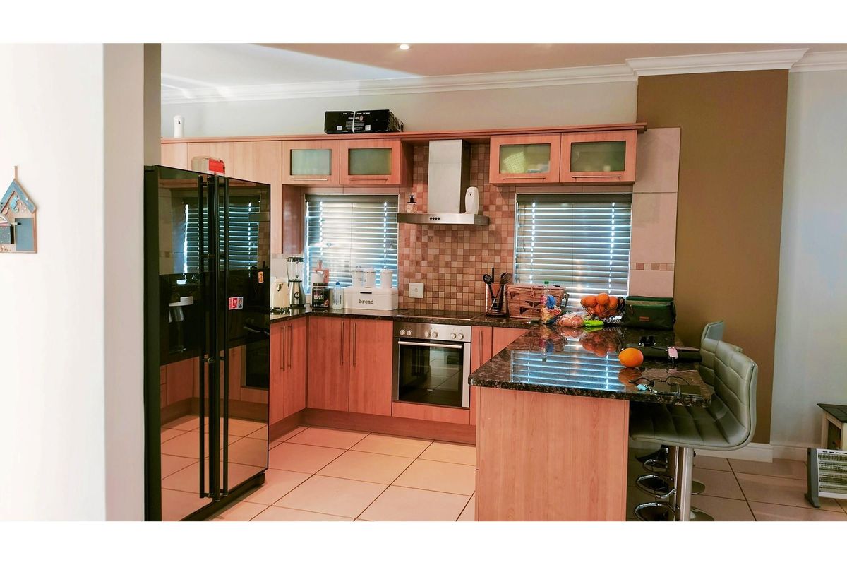 A functional kitchen featuring wood-finish cabinetry, granite countertops, a breakfast bar, built-in oven, extractor fan, and tiled flooring.