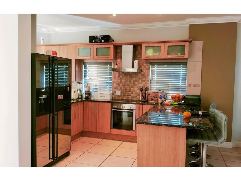 A functional kitchen featuring wood-finish cabinetry, granite countertops, a breakfast bar, built-in oven, extractor fan, and tiled flooring.