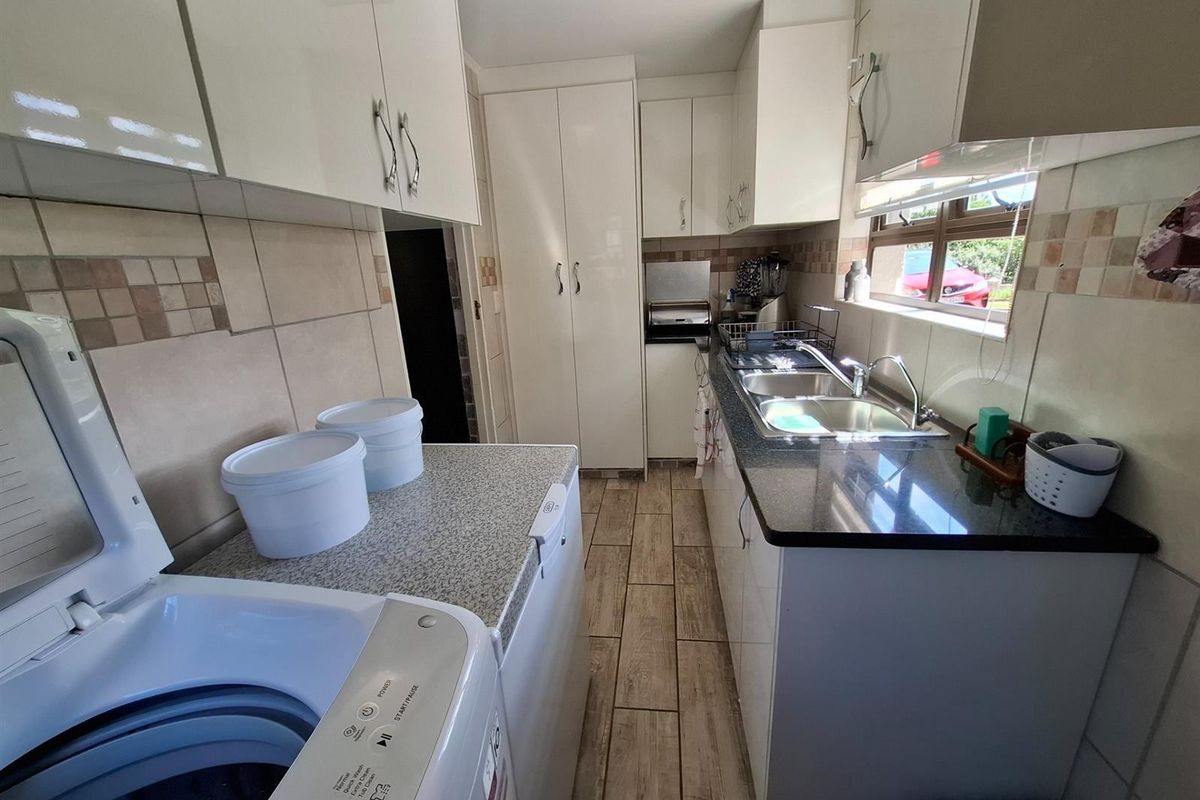Functional kitchen and laundry area featuring built-in cabinetry, granite countertops, double basin sink, and tiled flooring.