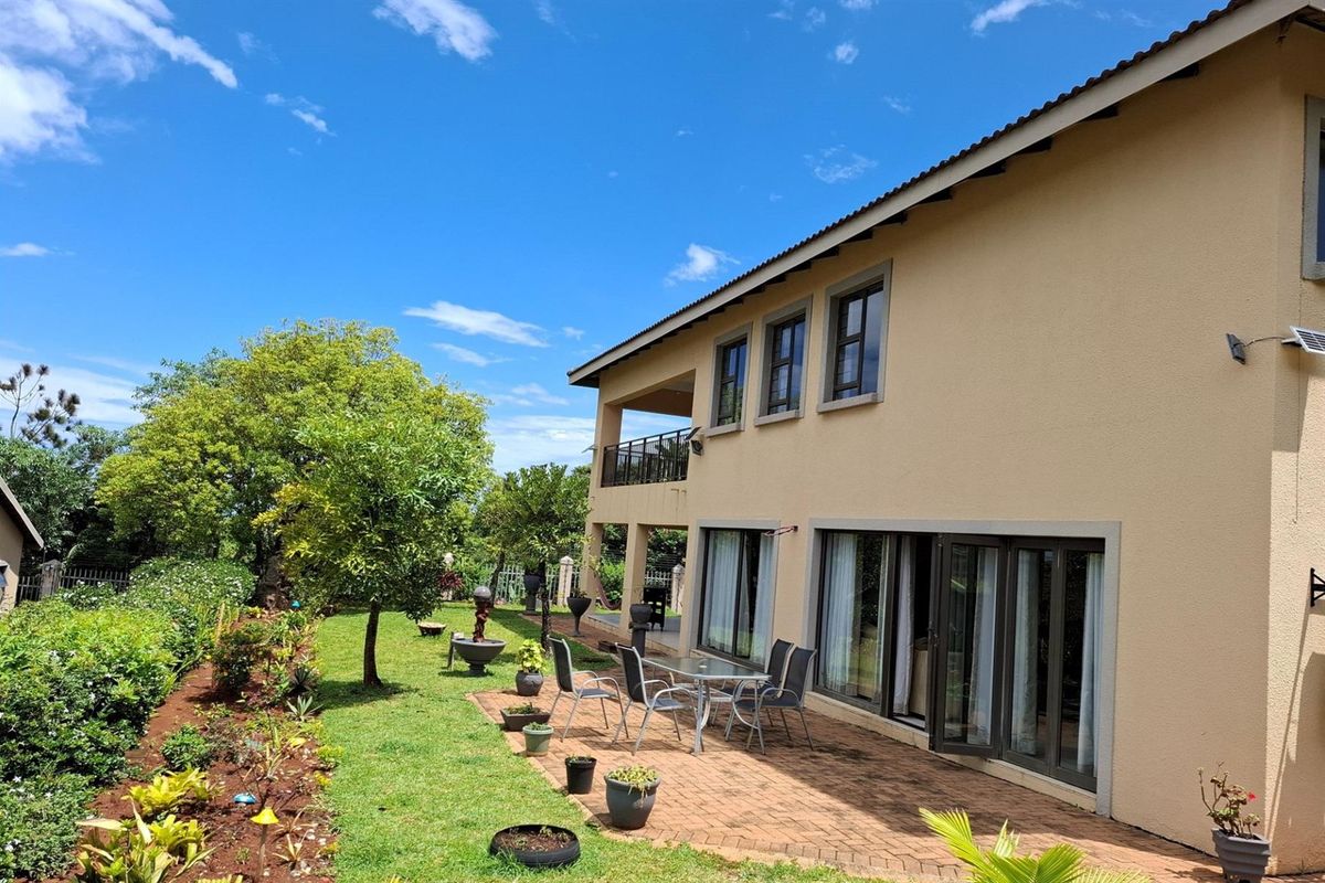 Rear view of the townhouse featuring a paved patio area, landscaped garden, and a covered balcony on the upper level.