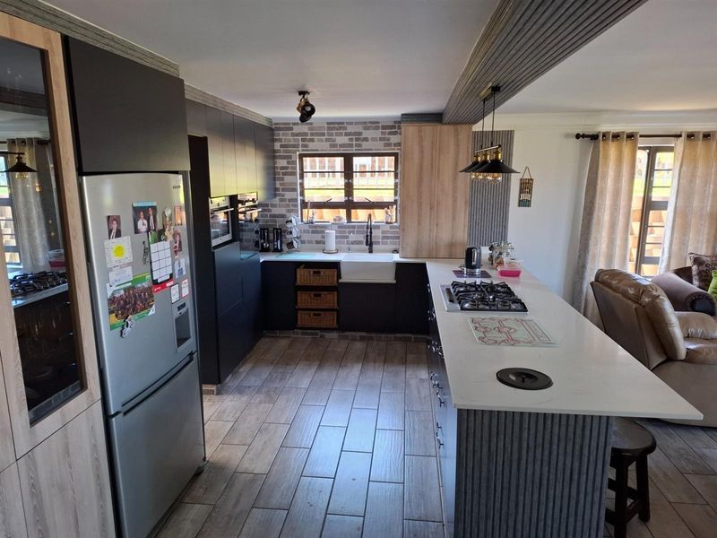 Modern open-plan kitchen featuring dark cabinetry, a central island with a gas hob, stone countertops, and a farmhouse-style sink with brick-effect backsplash.