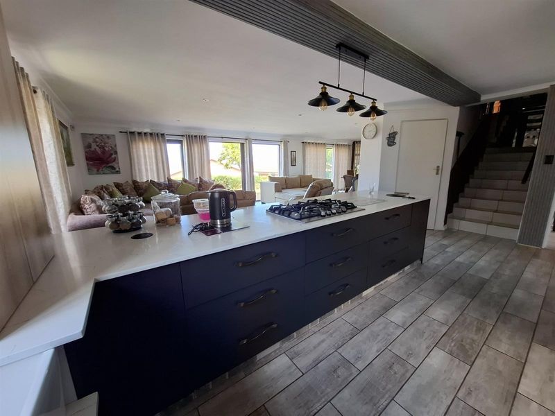 Open plan living area featuring a modern kitchen island with a built-in gas hob, sleek cabinetry, and tiled flooring, seamlessly connecting to the lounge.