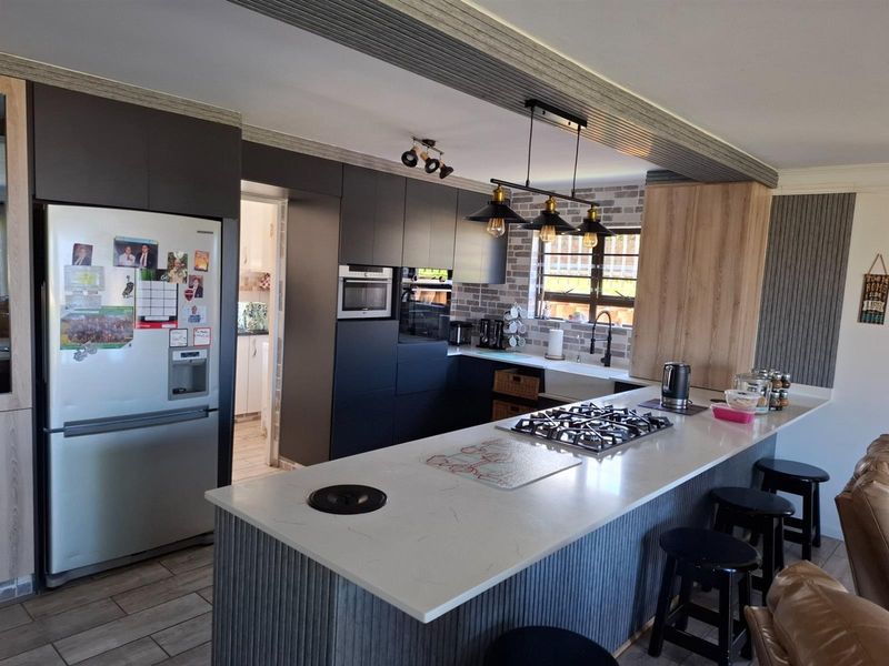 Modern open-plan kitchen featuring a large island with a built-in gas hob, stone countertops, dark cabinetry, and a farmhouse-style sink.