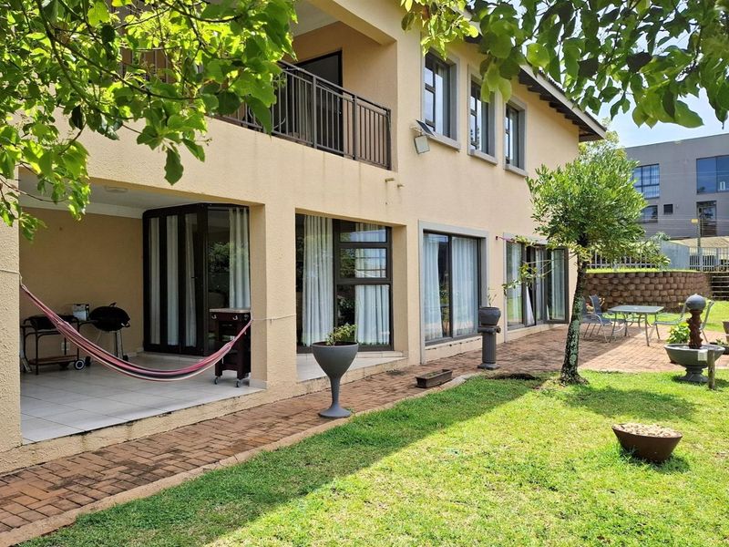 Rear view of the townhouse featuring a covered patio, paved walkway, and a well-maintained garden area with established landscaping.