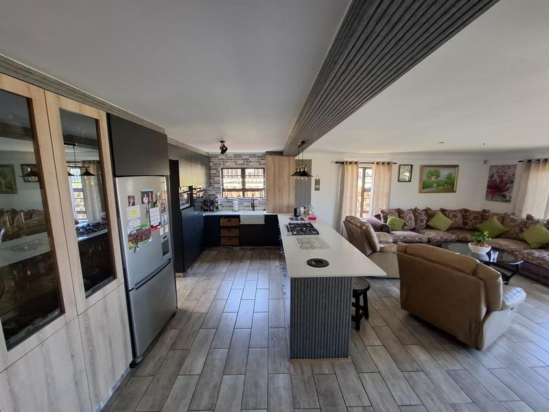 Open-plan living area featuring a modern kitchen with a central island, gas hob, and tiled flooring, seamlessly flowing into the adjacent lounge space.