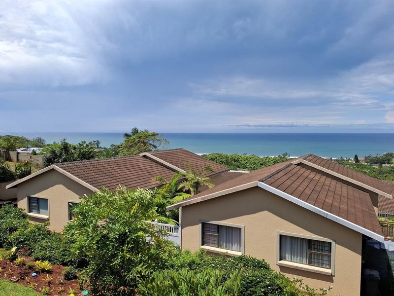 Elevated view of the townhouse complex rooftops featuring tiled roofing and a scenic ocean horizon in the background.